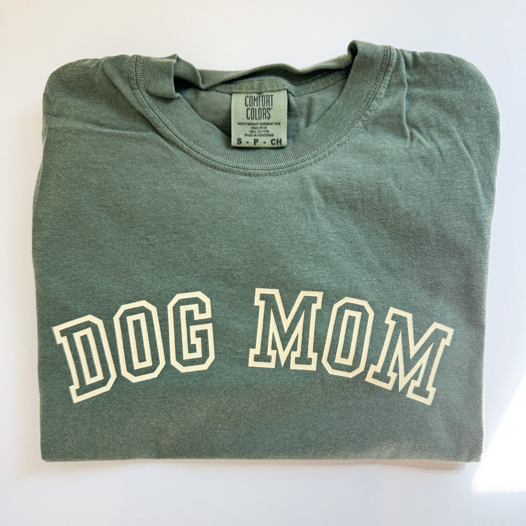 Folded green t-shirt with 'DOG MOM' text on a white background